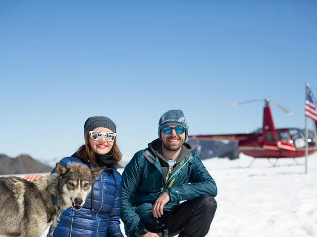 Couple posing with sled dog and helicopter on snow-covered Knik Glacier