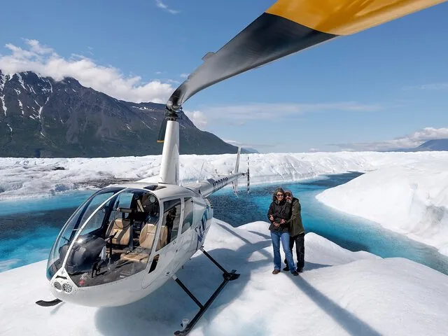 Helicopter landed on Knik Glacier with two passengers standing nearby