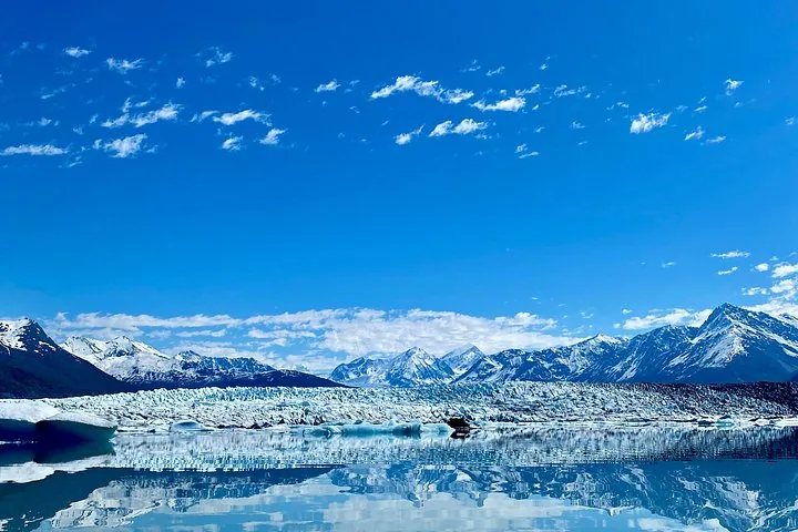 Panoramic view of a glacier and snow-capped mountains reflecting in calm water