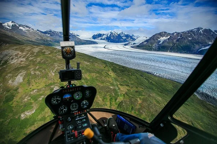 View from inside a helicopter flying over a vast glacier and mountains.