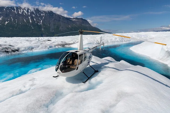 White helicopter parked on a glacier next to a blue meltwater pool