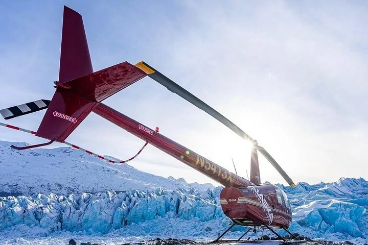 Red helicopter parked on jagged blue glacier ice under a sunny sky